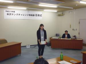 カーディガンを着た女性が正面に立ち、紙を持ちながら笑顔で参加者に向けて自己紹介をしている様子の写真