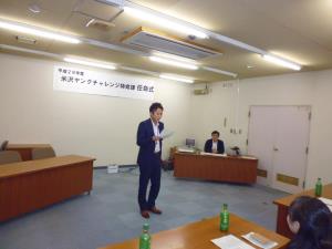 スーツ姿の男性が正面に立ち、白い紙を見ながら参加者に向けて自己紹介をしている様子の写真