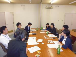 班ごとに分かれた8人の参加者が長机を囲むように座り、顔を合わせながらミーティングをしている写真