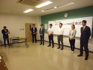 会場正面に6名の男女が横一列に並び、司会者のかたに紹介されている様子の写真