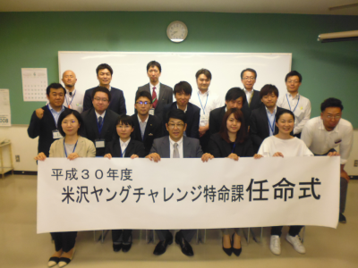 横3列になって並ぶ関係者が記念撮影をしており、1列目に座る5名の方が「平成30年度 米沢ヤングチャレンジ特命課任命式」と書かれた大きな紙を一緒に持っている写真
